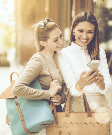 Two women walking down the street looking at a cell phone